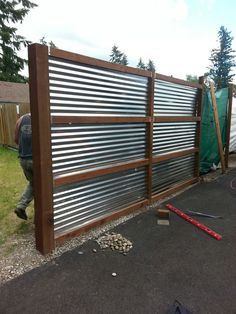 a man standing next to a metal fence in the middle of a yard with tools laying on the ground