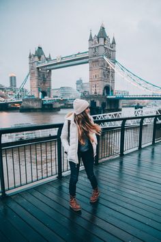 a woman is standing on a bridge looking at the water and tower bridge in the background