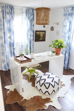 a white desk sitting in front of a window next to a potted plant on top of a rug