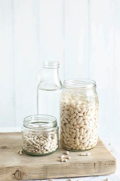 two jars filled with white beans sitting on top of a wooden table next to a glass bottle