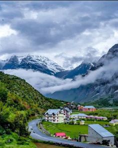 the mountains are covered in clouds and green grass, while houses sit on either side of a winding road