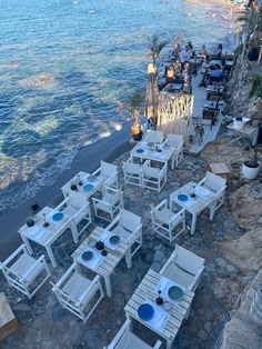 tables and chairs are set up on the beach for an outdoor dining area with water in the background