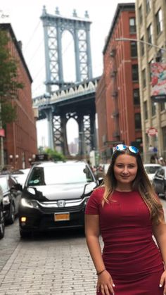 a woman in a red dress is standing on the sidewalk with cars and buildings behind her