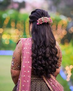 the back of a woman's head wearing a pink and gold sari with flowers in her hair