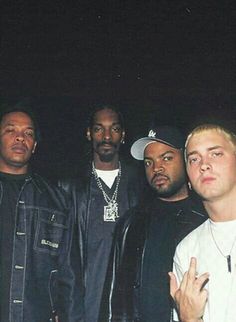 a group of men standing next to each other in front of a dark background with one pointing at the camera