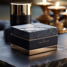 a black and gold box sitting on top of a marble table next to two candles