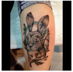 a rabbit tattoo on the leg of a woman's leg, with leaves around it