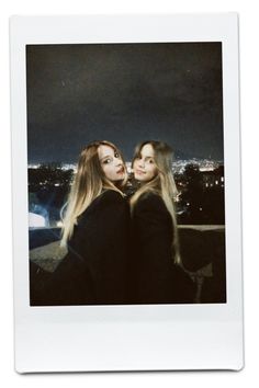 two young women standing next to each other in front of a city skyline at night