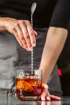 a person holding a spoon over a glass filled with liquid and orange slices in it