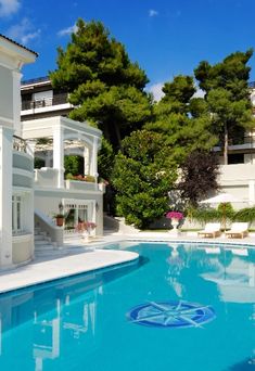 an empty swimming pool in front of a large white building with balconies and trees