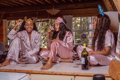 three women dressed in pink robes sitting on a table with wine glasses and bottles next to each other