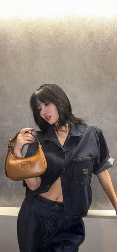 a woman in black shirt and jeans holding a brown purse with her right hand on her hip