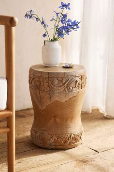 a vase with flowers on top of a wooden table next to a chair and window