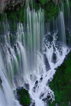 the water is flowing over the rocks and green mossy plants on the side of the waterfall