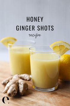 two glasses filled with honey ginger shots on top of a wooden table next to sliced lemons