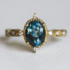 Like something from a magical land, this unique vintage-inspired London Blue Topaz ring goes by the name of Amelia. It is a perfect ring for anyone looking for a special and breathtaking ring and loves delicate jewelry that still wows you. Details Center Gemstone: London Blue Topaz Stone Shape: Oval Measurements: approx. 9x7mm Total carat weight: 2.5ct Side stone: round Moissanite Measurements: approx. 1.7mm, 1.5mm Band measurements: approx. 1.8mm wide, approx. 1.5mm thick Pictured in vermeil, a Yellow Topaz Ring, Planet Ring, Magical Land, Moss Agate Ring, London Blue Topaz Ring, Blue Topaz Stone, Rose Quartz Ring, Swiss Blue Topaz, Agate Ring