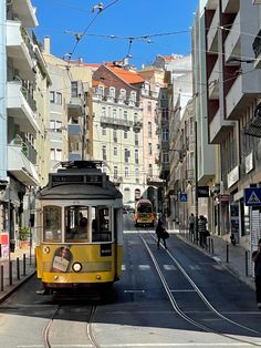 a yellow trolley car traveling down a street next to tall buildings and people walking on the sidewalk