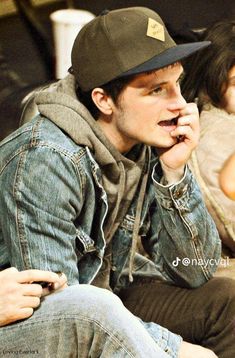 a young man sitting on top of a couch talking on a cell phone while wearing a hat