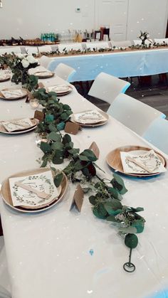 the table is set with place settings and greenery on each plate, along with napkins