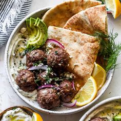 two bowls filled with meatballs, pita bread and garnished with herbs