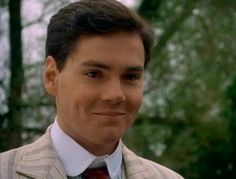 a man in a suit and tie smiling at the camera with trees in the background