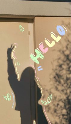 the shadow of a person standing in front of a wall with writing on it and a tree