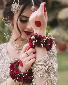 a woman with red and white makeup holding her hands up to her face while wearing jewelry