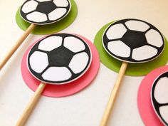 four cupcake toppers with soccer balls on them and wooden sticks in the middle