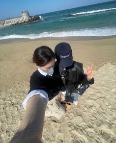 two people standing on top of a sandy beach next to the ocean with their hands in the air