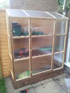 a wooden greenhouse with glass doors on the outside and shelves full of plants in it