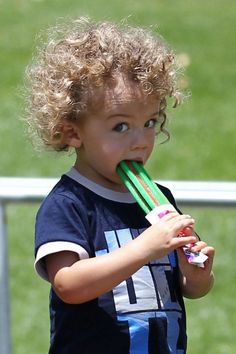 a young boy holding a green toothbrush in his mouth while standing on a soccer field