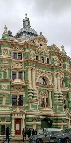 people are walking in front of an old building that is green and white with gold trim