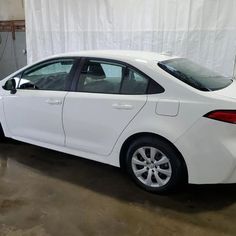 a white car parked in a garage next to a white wall with curtains on it