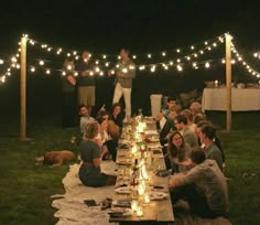 a group of people sitting around a long table with lights strung over it and food on the table