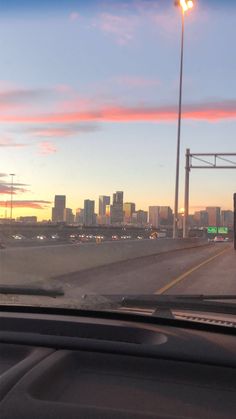 the sun is setting over a city skyline as seen from inside a moving car window