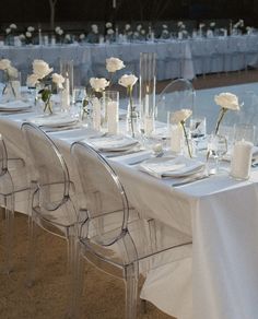 the table is set with clear chairs and white linens