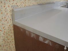 a white counter top in a kitchen with floral wallpaper and a brown cabinet under it