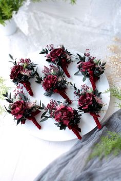 a white plate topped with red flowers on top of a table next to greenery