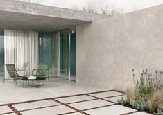 an empty patio with chairs and plants on the ground next to a concrete wall that has sliding glass doors