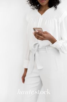 a woman in white is looking at her cell phone while standing with her hands on her hips