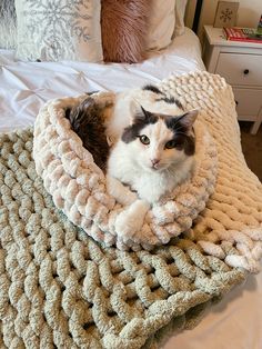 a cat sitting in a crocheted bed on top of a blanket