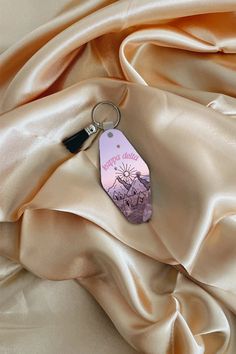 a pink keychain with the word hello written on it sitting on a satin fabric