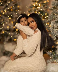 a woman holding a baby in front of a christmas tree with lights on the trees