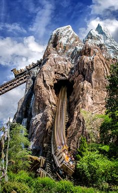 a roller coaster going down a mountain with people on it's side in the background