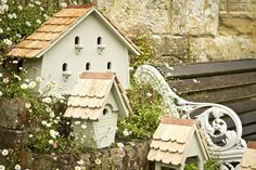 two bird houses sitting on top of a stone wall next to a bench and flowers