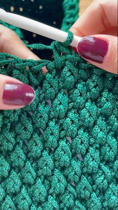 a woman is crocheting the stitchs on her green knitted afghan with a white crochet hook