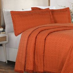 a bed with an orange bedspread and pillows on top of it, next to a night stand