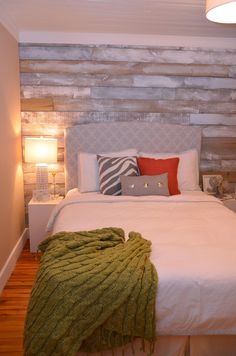 a bed with white sheets and pillows in a bedroom next to a wall made out of wood planks