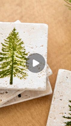 three white coasters with green trees on them sitting on top of a wooden table