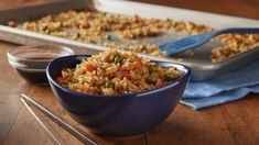 a blue bowl filled with rice and vegetables next to a pan of dipping sauces